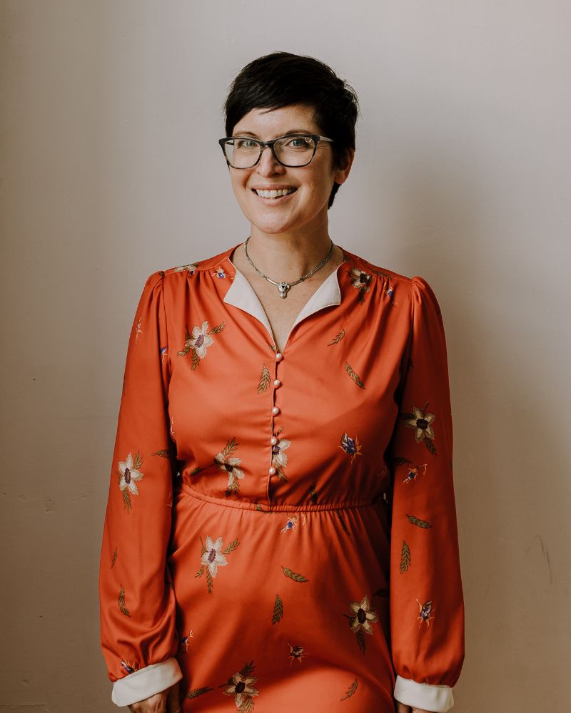 Photo of author Erica Richmond, wearing an orange silk dress. She is smiling directly at the camera, preparing to speak to a group.