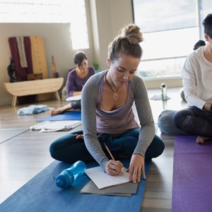 Woman sits on a yoga mat and writes in a journal during a pilates class.